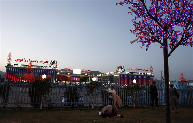 FILE - In this June 9, 2011, file photo Afghan men pray outside a wedding hall in Kabul, Afghanistan. The frosted-glass wedding halls in Kabul appear like a neon dream of what Afghanistan could be amid the ruined roads and bullet-marred apartment buildings. And some believe the weddings that cost of tens of thousands of dollars hint at the graft strangling government and private life in Afghanistan.(AP Photo/Gemunu Amarasinghe).