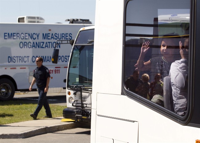 A young forest fire evacuee waves to firefighters from the window of a transport bus as they leave The Aviation Centre of Excellence in Thunder Bay, Ontario on Friday July 22, 2011. THE CANADIAN PRESS/Frank Gunn.