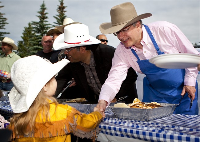 Prime Minister Stephen Harper, right, shakes hands with Ashleigh Budd, four, as he dishes out pancakes at Stampede breakfast in Calgary, Alta., Sunday, July 10, 2011.THE CANADIAN PRESS/Jeff McIntosh.