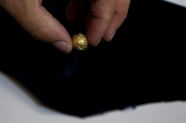 A worker for the IAA, Israel's Antiquities Authority holds a gold bell found in Jerusalem, Sunday, July 24, 2011. The tiny golden bell preserved for two millennia underneath Jerusalem is ringing again, having been discovered by Israeli archaeologists excavating a Roman-era sewer. (AP Photo/Sebastian Scheiner).
