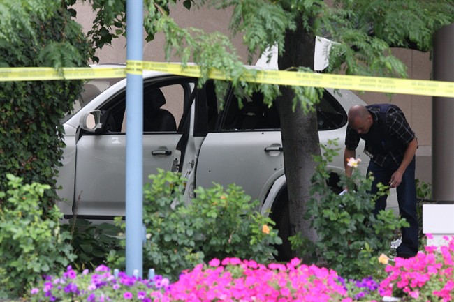 An RCMP member collects evidence near a bullet-riddled SUV after a masked gunman open fire on a luxury car outside an upscale hotel in a tourist area of Kelowna, B.C. on Sunday, Aug. 14, 2011. Six people were taken to hospital. THE CANADIAN PRESS/Chris Stanford.