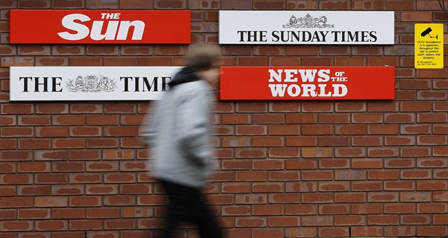 FILE - This is a Thursday, Jan. 27, 2011 file photo of a pedestrian he passes signs at the entrance to News International in Wapping, London. (AP Photo/Kirsty Wigglesworth, File).