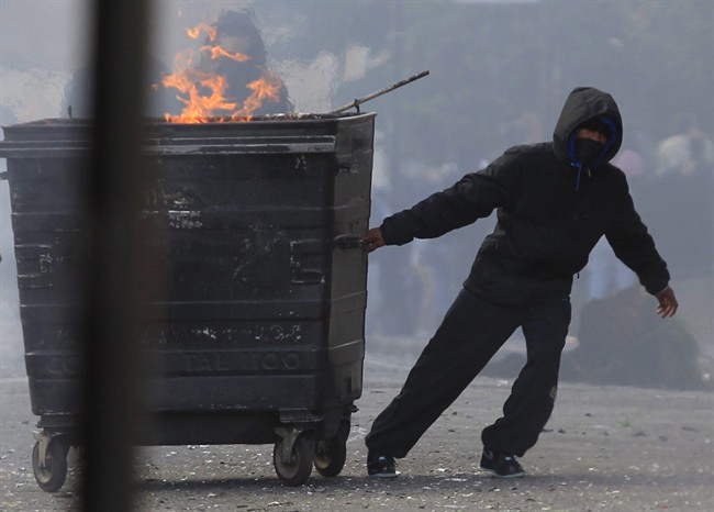 FILE - In this Monday Aug. 8, 2011 file photo a masked youth pulls a burning garbage bin set on fire by rioters in Hackney, east London. More than two weeks after the end of riots in London and other English cities, Britain's government and police met social media executives Thursday to discuss how to prevent their services from being used to plot violence. (AP Photo/Lefteris Pitarakis, File).