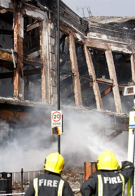 Firefighters look at a burned-out building in Tottenham, north London, Sunday, Aug. 7, 2011, after a demonstration against the death of a local man turned violent and cars and shops were set ablaze. One police officer was hospitalized and seven others were injured during riots after a north London suburb exploded in anger Saturday night following a gathering to protest the Thursday shooting by police of the 29-year-old. (AP Photo/Akira Suemori).