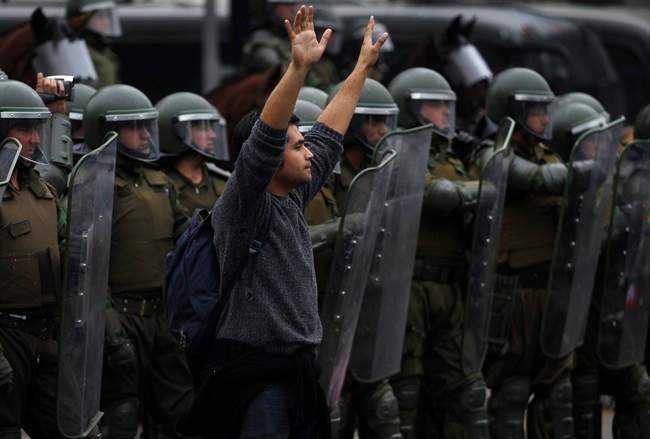 A demonstrator holds up his hands as a signal to rock-throwing protestors to stop throwing rocks at riot police on the second day of a national strike in Santiago, Chile, Thursday Aug. 25, 2011. Chileans marched Thursday, demanding profound changes in the country's heavily centralized and privatized form of government. Union members, students, government workers and Chile's center-left opposition parties joined the nationwide two-day strike. (AP Photo/Roberto Candia).