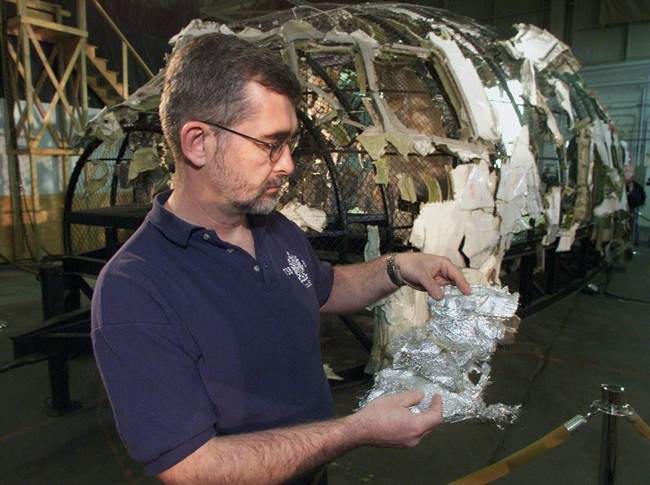 Transportation Safety Board senior investigator Don Enns displays metalized Mylar insulation material in front of the partially reconstructed cockpit of Swissair Flight 111 at a news conference in Halifax on Dec. 4, 2000. A former RCMP officer who investigated the crash of Swissair Flight 111 off Nova Scotia says officials didn't pursue suspicions an incendiary device brought down the plane. THE CANADIAN PRESS/Andrew Vaughan.
