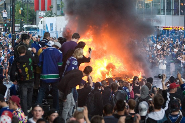 People watch a car burn during a riot following game 7 of the NHL Stanley Cup final in downtown Vancouver, B.C., on Wednesday, June 15, 2011.