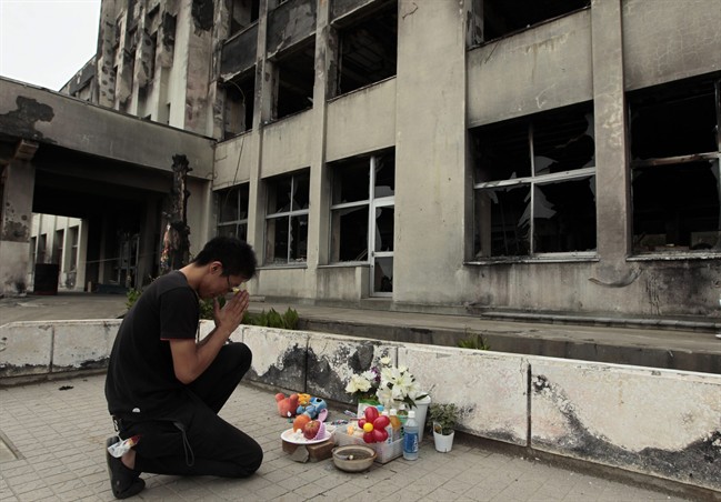 Yuki Omori, 23, prays at a makeshift shrine at Kadowaki Elementary School in Ishinomaki, northeastern Japan, Sunday, Sept. 11, 2011, six months after the March 11 earthquake. The college junior volunteers to make balloons at different kindergarten and elementary schools in the devastated area. (AP Photo/Hiro Komae).