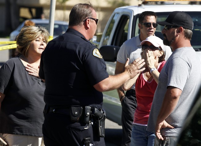 In this FILE photo, a police officer talks to onlookers near the site where six people were killed and three were wounded in a shooting at a hair salon in Seal Beach, Calif., Wednesday, Oct. 12, 2011.