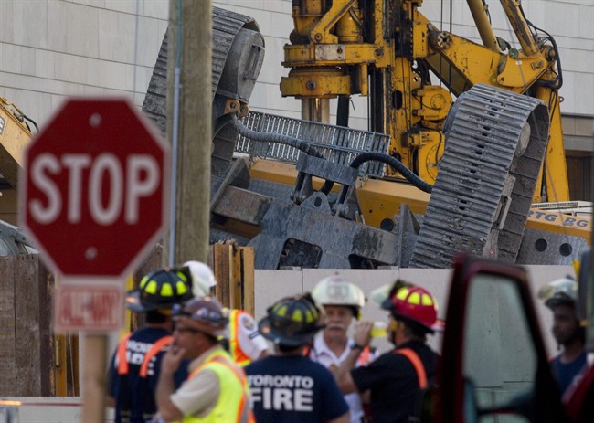 Members of the Fire Department stand in front of the upended tracks of the Vertical Drilling Machine which toppled over on a construction site at Toronto's York University campus, killing one worker and injuring five others on Tuesday, October 11, 2011. THE CANADIAN PRESS/Chris Young.