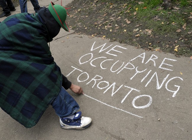 A protester writes on a sidewalk in a staging area at a downtown church grounds in Toronto, Sunday, October 16, 2011. After spending their first night camped outdoors in protest, Canadians who gathered to decry corporate greed and social inequality used Sunday to hammer out their action plan for the coming week. THE CANADIAN PRESS/J.P. Moczulski.