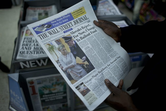 A worker poses for photographs by holding a copy of Wednesday's Wall Street Journal newspaper above a stand with stacks of other newspapers inside a newsagents at Victoria train station in London, late Wednesday, Oct. 12, 2011. The Guardian newspaper reported Wednesday that it had seen emails and documents showing that The Wall Street Journal funneled money through third parties to a company that was buying up copies of the Journal and boosting its European circulation. (AP Photo/Matt Dunham).