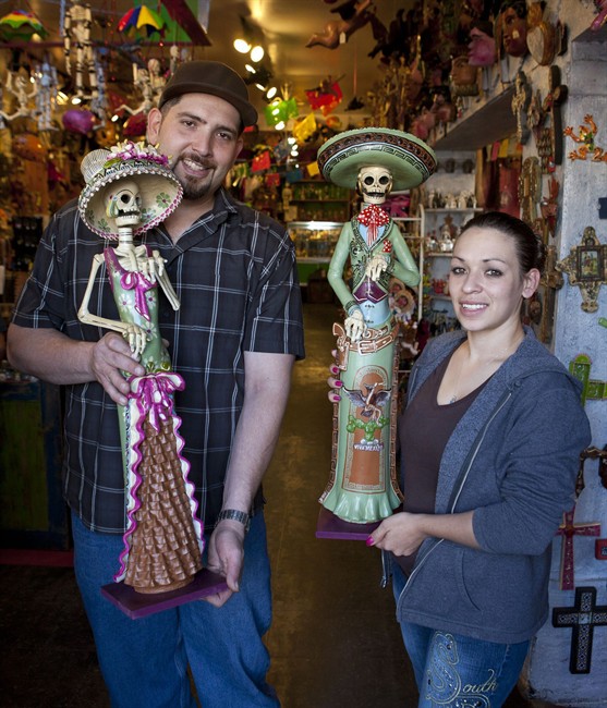 In this Monday, Oct. 3, 2011 photo, Kiko Torres, left, and his girlfriend Marlysa Sanchez, each hold a Catrina Day of the Dead doll inside Torres' store, Masks y Mas, in Albuquerque, N.M. The shop sells Day of the Dead art and clothing year-round. (AP Photo/Jake Schoellkopf).