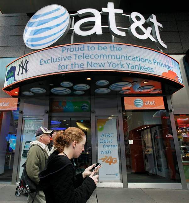 In this Oct. 18, 2011 photo, a woman using a cell phone passes an AT&T store, in New York. AT&T Inc. on Thursday, Oct. 20, 2011, reported a decline in the number of iPhones activated in its latest quarter, as buyers waited for the new model. ((AP Photo/Mark Lennihan).