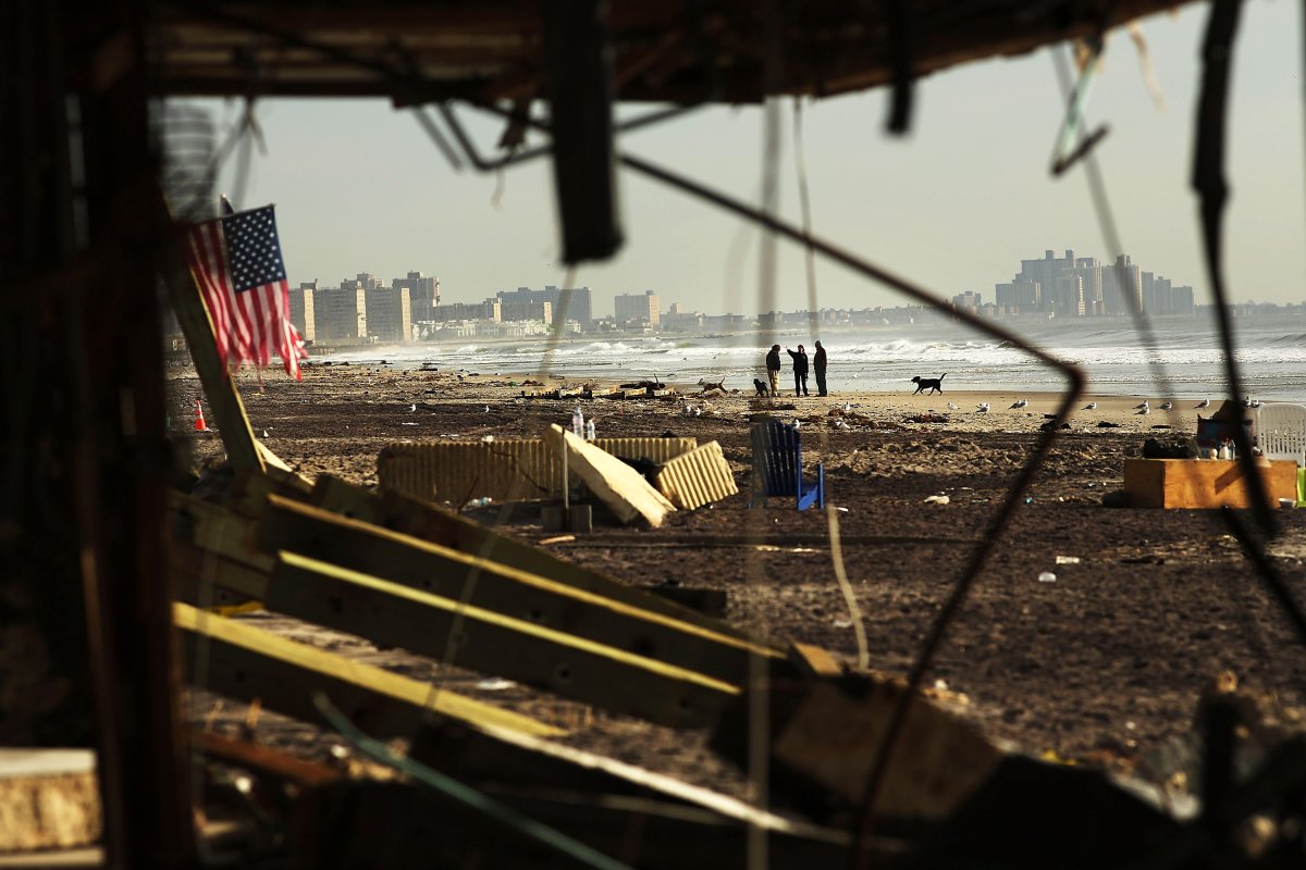 NEW YORK, NY - People walk along a beach amidst debris in the heavily damaged Rockaway neighborhood where a large section of the iconic boardwalk was washed away .