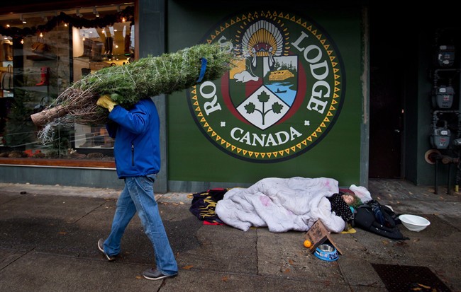 A man carries a Christmas tree to as a homeless man sleeps on the sidewalk in Vancouver, B.C., on December 10, 2012. THE CANADIAN PRESS/Darryl Dyck.