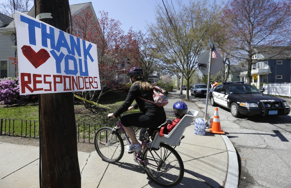A woman with a child passenger rides a bicycle past the entrance to Franklin St., in Watertown, Mass., Thursday, April 25, 2013, not far from where Boston Marathon bombing suspect Dzhokhar Tsarnaev was caught hiding in a boat Friday, April 19.