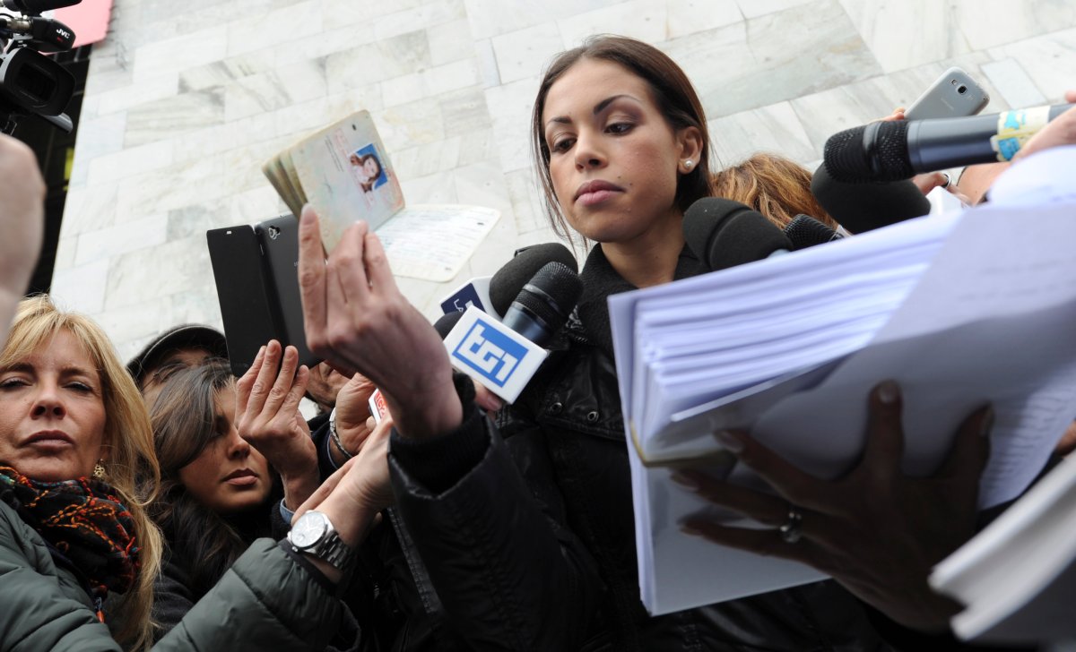 Karima el-Mahroug, also known as Ruby, bottom left, a Moroccan woman at the center of ex-Premier Silvio Berlusconi's sex-for-hire trial, holds up her passport in one hand and a stack of papers in the other as she is mobbed by reporters outside Milan's court house, Italy, Thursday, April 4, 2013. 