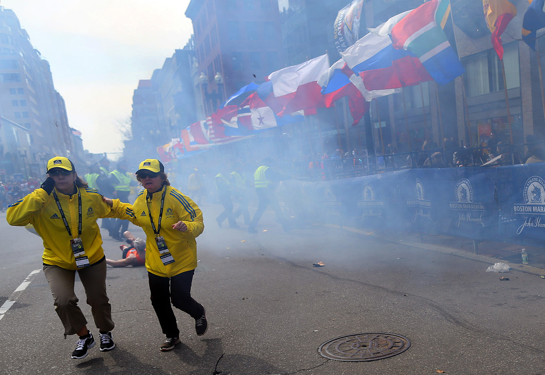 Two officials run away from the first explosion, right, on Boylston Street at the 177th Boston Marathon, April 15, 2013.