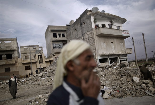 In this Wednesday, Dec. 12, 2012 file photo, an elderly Syrian man smokes a cigarette as he stands next to a residential building destroyed in a government airstrike, in Maaret Misreen, near Idlib, Syria. (AP Photo/Muhammed Muheisen, File).