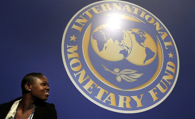 A woman sits in front of an International Monetary Fund logo at a meetin , Oct. 10, 2012 in Tokyo.