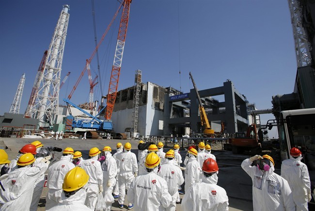 FILE - In this March 6, 2013 file photo, journalists wearing protective gears are escorted to the damaged No. 4 reactor building and an under construction foundation, center right, which will store the reactor's melted fuel rods, at Tokyo Electric Power Co.'s crippled Fukushima Dai-ichi nuclear power plant in Okuma town, Fukushima prefecture, northeast of Tokyo. The cooling system failed for a storage pool for fuel at one of the reactors at the tsunami-damaged nuclear plant in northeastern Japan Friday, April 5, 2013, - the second in a month, although there was no immediate danger from the breakdown. (AP Photo/Issei Kato, File).