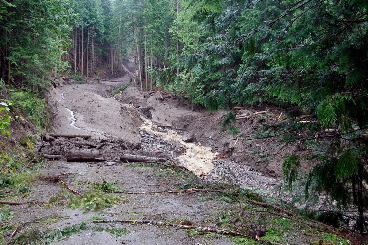 Debris covers a road Sunday, July 15, 2012 that was torn away by a landslide that buried three homes and has left four people unaccounted for in Johnsons Landing, B.C. THE CANADIAN PRESS/Jeff McIntosh.