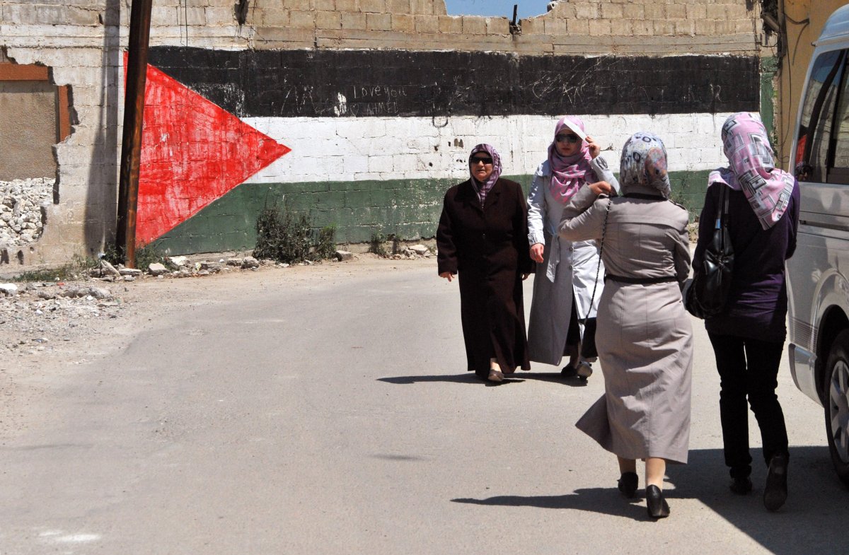 Women walk past a giant Palestinian flag painted on a wall at a camp for Palestinian refugees on May 22, 2013 in Homs, Syria. The conflict in Syria has displaced more than two-thirds of Palestinian refugees living in the country, the UN Relief and Works Agency for Palestine refugees said.    
