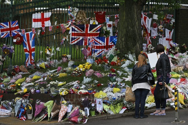 People look at some of the thousands of floral and other tributes left in honour of murdered 25-year-old British soldier Lee Rigby, at the scene near Woolwich Barracks in London, Wednesday, May 29, 2013. Two men attacked and killed the off-duty soldier in broad daylight, Wednesday, May 22. They were shot by police and arrested on suspicion of murder. (AP Photo/Lefteris Pitarakis).