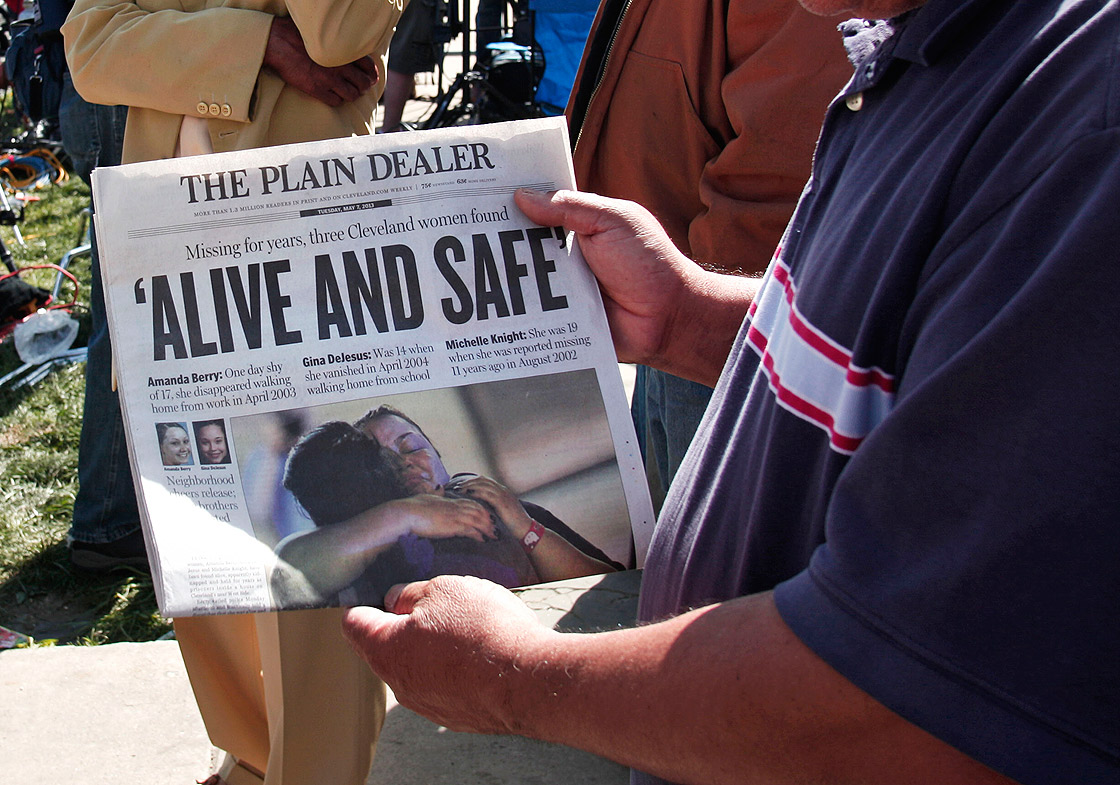 A man shows page one of The Plain Dealer newspaper to a friend while people gather along Seymour Avenue near the house where three women, who disappeared as teens about a decade ago, were found alive, May 7, 2013 in Cleveland, Ohio. 