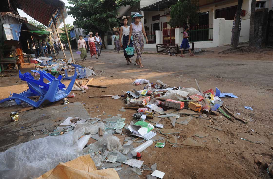 People walk past debris scattered outside a shop after riots broke out in a village at Oakkan town, some 100 kilometres north of Yangon on May 1, 2013. 