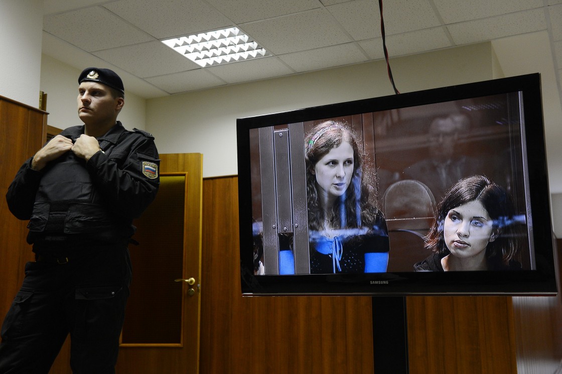 A police officer stands near a screen showing j two of the jailed members of the all-girl punk band "Pussy Riot," (L-R) Maria Alyokhina and Nadezhda Tolokonnikova sitting in a glass-walled cage in a court in Moscow, on October 10, 2012.