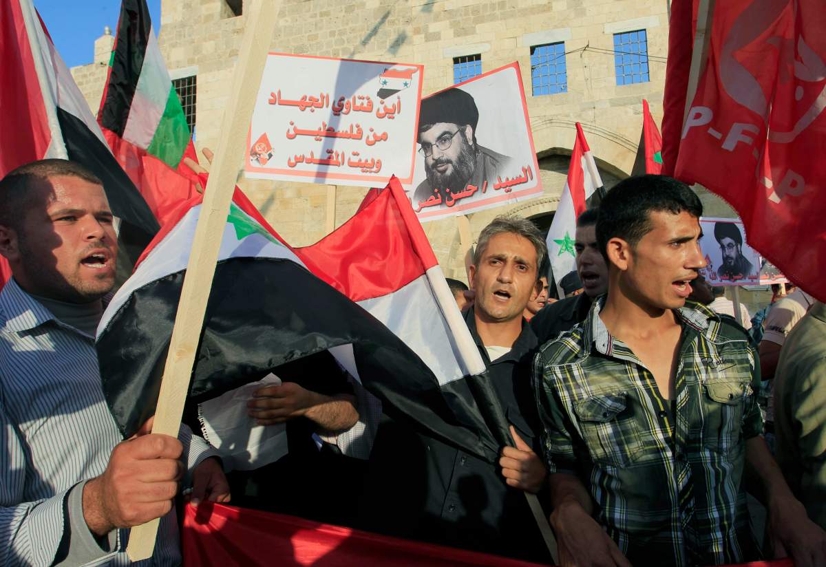 Palestinian supporters of the Popular Front for the Liberation of Palestine (PLFP) wave the group's red flag, the Syrian flag, and the Palestinian flag as they holds poster of Lebanon's Hezbollah leader Sheikh Hassan Nasrallah, during a rally on May 7,2013, against  Israeli attack on Syria in Khan Yunis town in the southern Gaza Strip. 