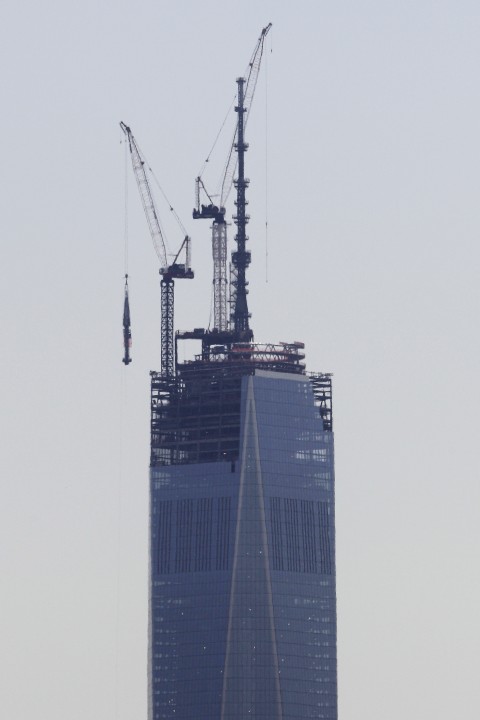 A 408-foot spire, left, is lifted toward the top of the construction of One World Trade Center seen from the Heights neighborhood of Jersey City, N.J., Thursday, May 2, 2013. The spire, which will put the building at 1,776 feet tall, will be placed on the structure at a later day. (Julio Cortez/AP Photo).