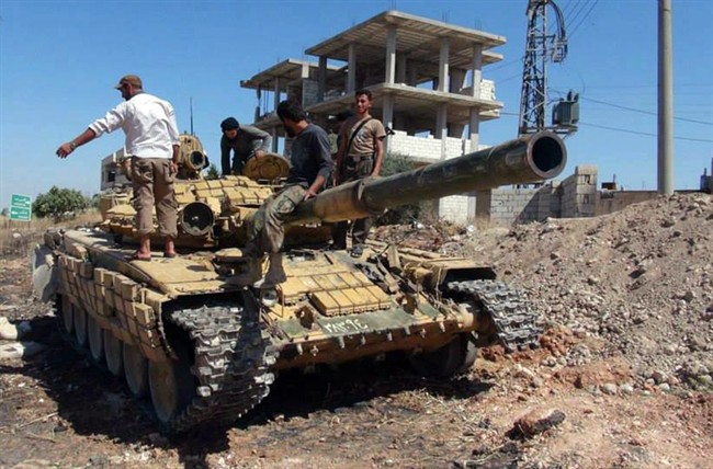 In this Friday, June 14, 2013 citizen journalism image provided by Edlib News Network, ENN, Syrian rebels stand on top of a tank they took after storming the Iskan military base in Idlib province, northern Syria. After weeks of fighting the rebels captured tanks as well as other vehicles and artillery in the area. 