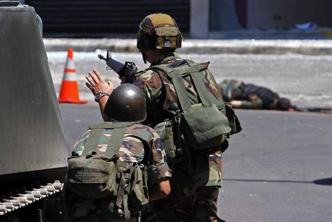 Lebanese army soldiers, take their positions behind an armoured vehicle, after clashes between followers of a radical Sunni cleric Sheik Ahmad al-Assir and Shiite gunmen, in the southern port city of Sidon, Lebanon, Sunday, June 23, 2013. 