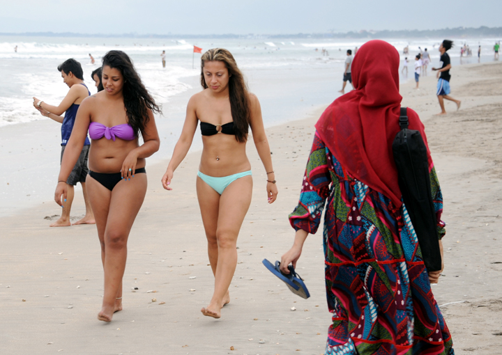 A Muslim woman (R) wearing a veil walks past foreign tourists wearing bikinis on Kuta beach near Denpasar on Indonesia's resort island of Bali on June 6, 2013.