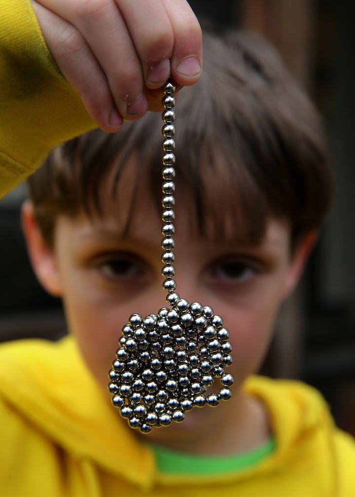 Brandon Bruski, 9, holds dozens of Buckyballs on Thursday, April 11, 2013.  In January, Brandon accidentally swallowed two balls from this set of the small magnetic desk toys. The magnets left Brandon with a small and large intestine bound together.  Emergency surgery was required. 