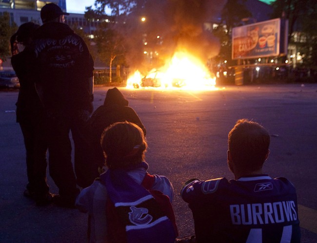 Vancouver Canucks fans watch as two police cars burn during a riot in downtown Vancouver, Wednesday, June 15, 2011 following the Vancouver Canucks 4-0 loss to the Boston Bruins in game 7 of the Stanley Cup hockey final. THE CANADIAN PRESS/Ryan Remiorz.
