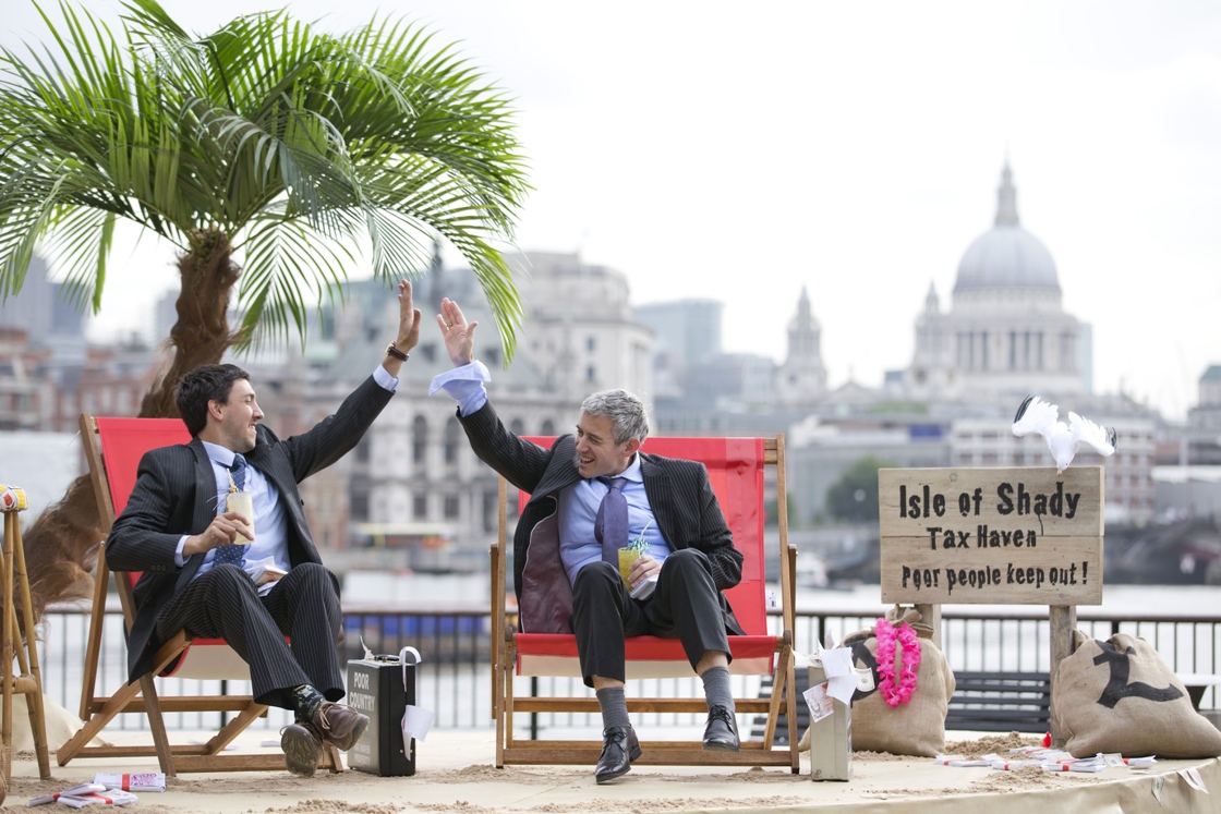 Protesters dressed as a businessman offer each other a high five on a protest site named as the "Isle of Shady Tax Haven.".