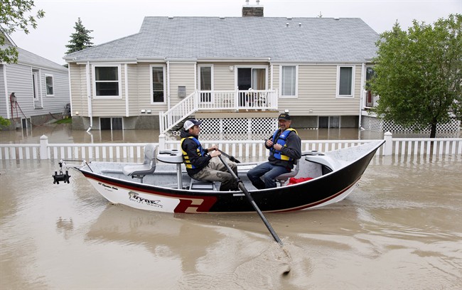 Two men use a fishing boat to rescue residents from a neighborhood after heavy rains caused flooding, closed roads, and forced evacuation in High River, Alta., Thursday, June 20, 2013. 