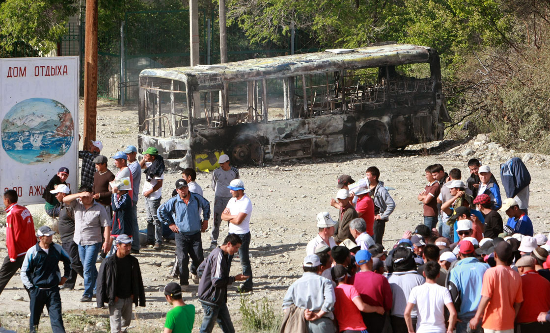 A picture taken on May 31, 2013, shows protesters walking in front of a burnt out bus near a power substation in the Kyrgyz village of Tamga, some 300 km southeast of the capital Bishkek. Parts of Kyrgyzstan were under curfew today after clashes between security forces and protesters who want the Kumtor Canadian-owned gold mine nationalised led the president to declare a state of emergency. The violence broke out after the arrests of dozens of demonstrators cut off power to the mine by switching off the power of the Tamga substation.
