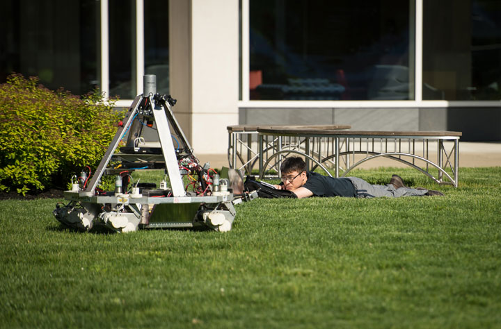 A Worcester Polytechnic Institute (WPI) student, lying in the campus quad reading, watches as the robot from the team of University of Waterloo approaches during the NASA 2013 Sample Return Robot Challenge, Tuesday, June 4, 2013, at the Worcester Polytechnic Institute (WPI) in Worcester, Mass.