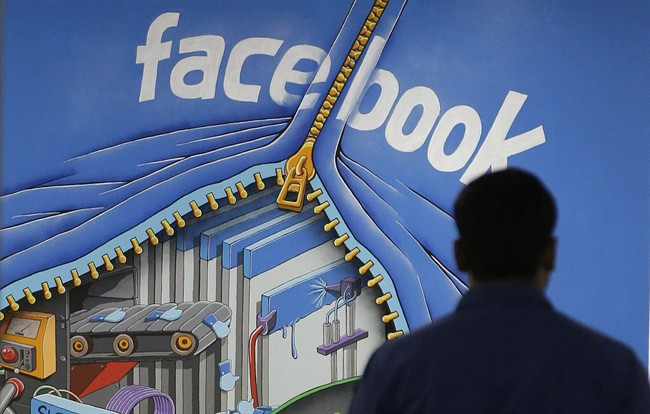 In this Friday, March 15, 2013 file photo, a Facebook employee walks past a sign at Facebook headquarters in Menlo Park, Calif. 