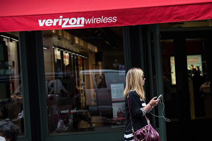 A woman uses her phone while walking past a Verizon Store on June 6, 2013 in the SoHo neighborhood of New York City. 