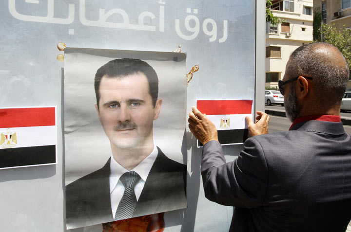 A Syrian man puts up images of the Egyptian flag next to a picture of Syrian President Bashar al-Assad as they protest in front of the old Egyptian Embassy in the capital Damascus, in solidarity with demonstrations in Egypt against Egypt's Islamist president on June 30, 2013. 