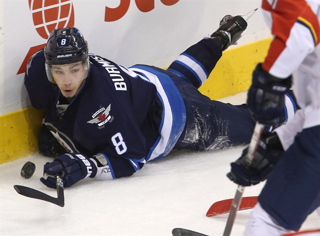 Winnipeg Jets' Alexander Burmistrov tries to play the puck after being tripped up behind the net during an NHL game in 2013.