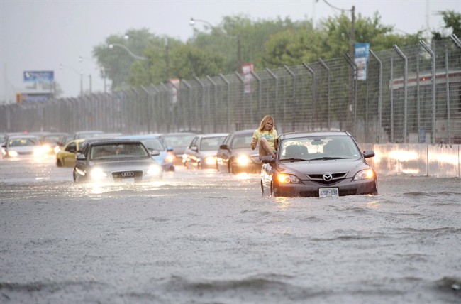 A woman gets gets out of her car to check it in flood water on Lakeshore West during a storm in Toronto on Monday, July 8, 2013. 