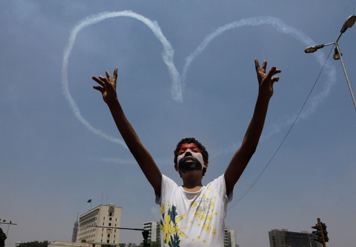 An Egyptian protester flashes v signs for military aircrafts forming a heart shape trails in the sky over Tahrir Square in Cairo, Egypt, Friday, July 5, 2013. 