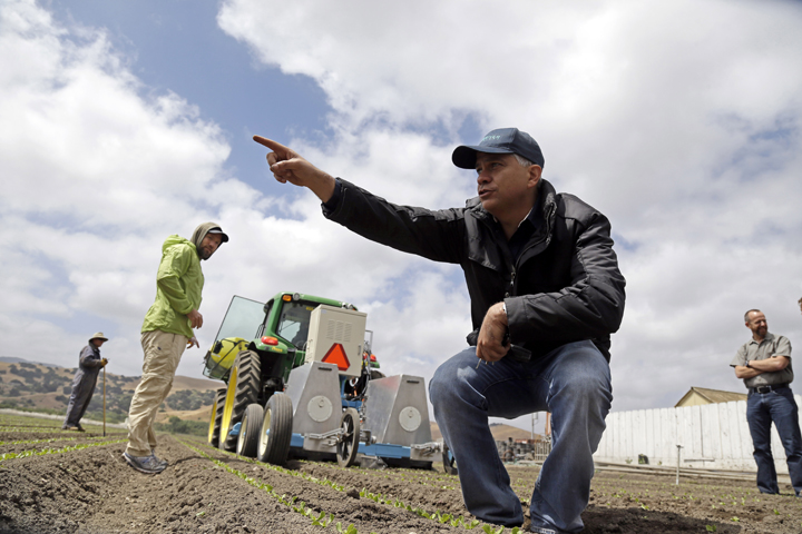 In this May 23, 2013, photo, Jorge Heraud, CEO of Blue River Technology, center, explains how the lettuce bot works as software engineer Willy Pell, in green, watches in Salinas, Calif. 